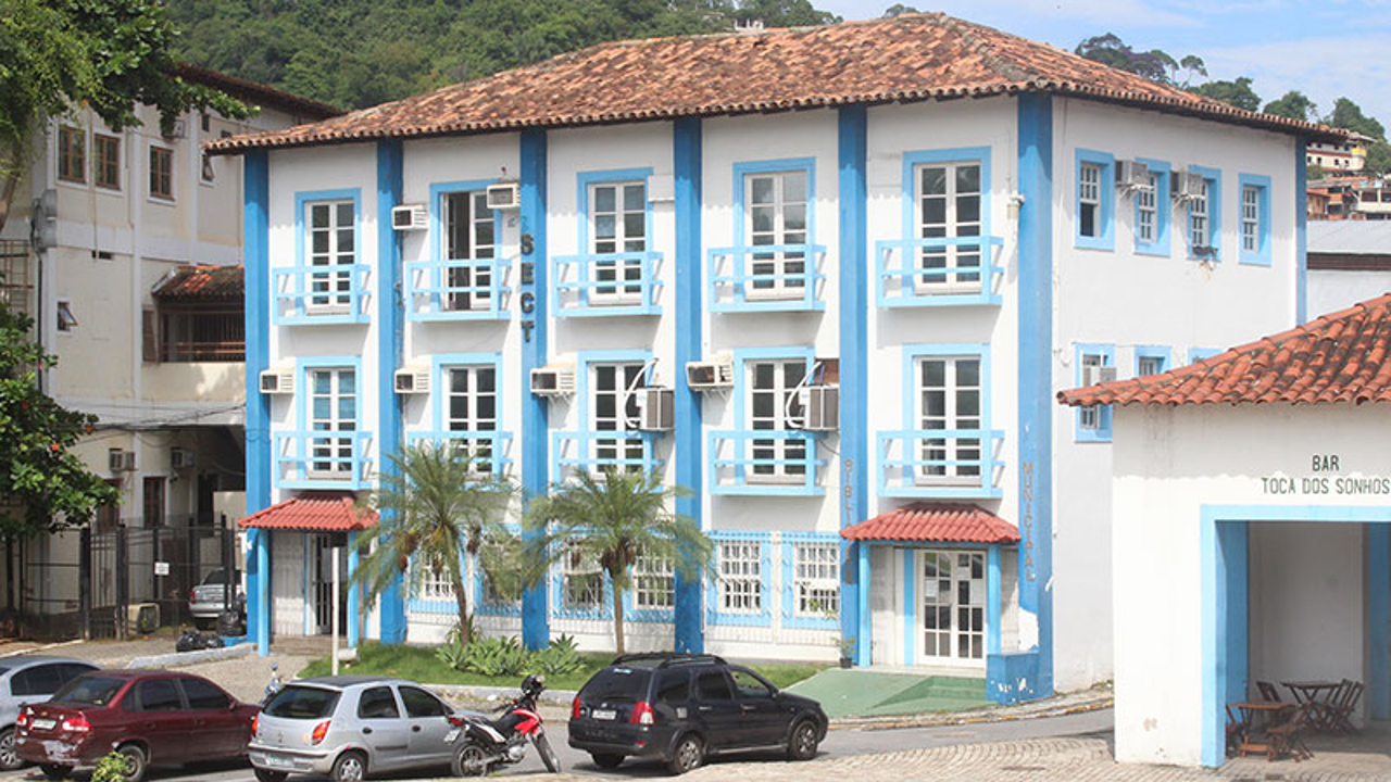 fachada do prédio da Prefeitura de Angra dos Reis com carros estacionados em frente e árvores ao redor