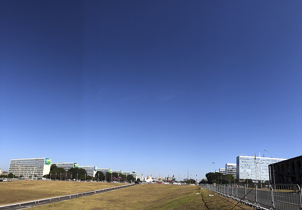 Vista da Esplanada dos Ministérios em Brasília com prédios governamentais ao fundo e céu azul